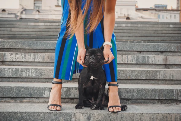 Black french bulldog puppy sitting on stairs between female legs — Free Stock Photo