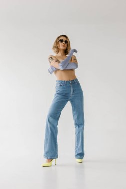 Beyaz arka planda kot pantolon ve eldiven giyen dövmeli seksi bir kadın.