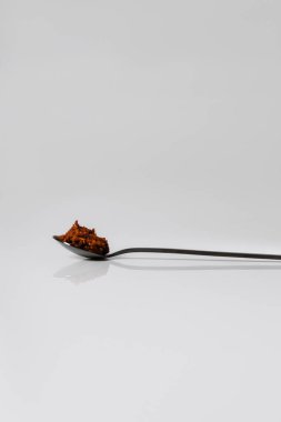 Beyaz arka planda siyah çay kaşığı biberli ev yapımı acı biber sosu eklentisi.