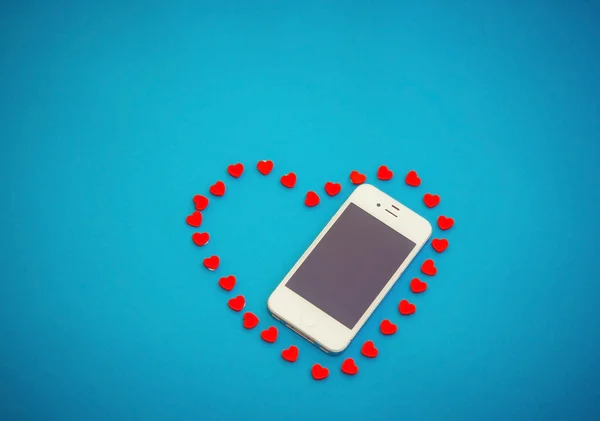 Vit telefon med röda hjärtan på blå bakgrund — Stockfoto