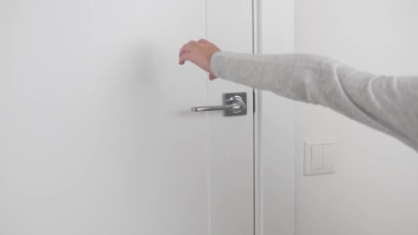A szőke fiú kinyitja a világos ajtót a kilincsnél fogva, és elhagyja a szobát. — Stock videók