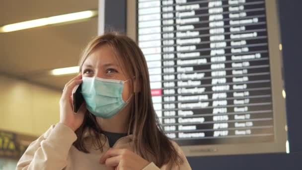 Una mujer con máscara médica habla por teléfono a la salida del aeropuerto. — Vídeos de Stock