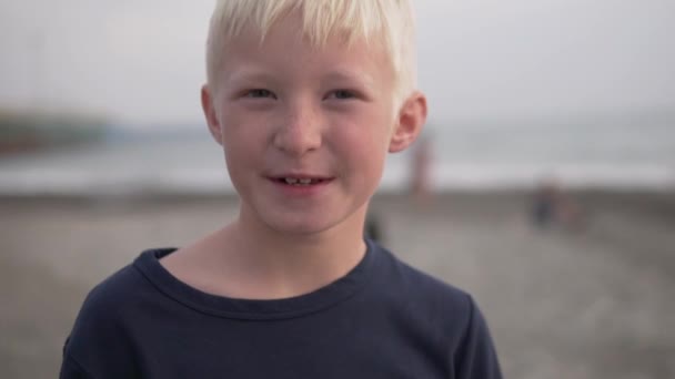 Primer plano de la cara de un hermoso chico rubio contra el mar — Vídeos de Stock