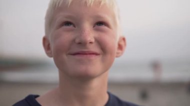 Mutlu sarışının yüzüne yakın çekim. Yüzünde deniz ve plajın arka planında çiller var.