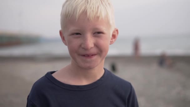 아름다운 금발의 소년의 얼굴이 씻겨진 바다와 해변의 배경에 근접 한 모습 — 비디오