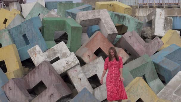 Een mooie vrouw in een strand rode jurk tegen een achtergrond van gekleurde stenen probeert te poseren voor een fotograaf — Stockvideo