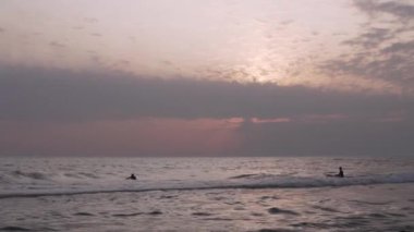 Gün batımında güzel denizde iki insan Soçi 'de küçük dalgalarda sörf yapıyor.