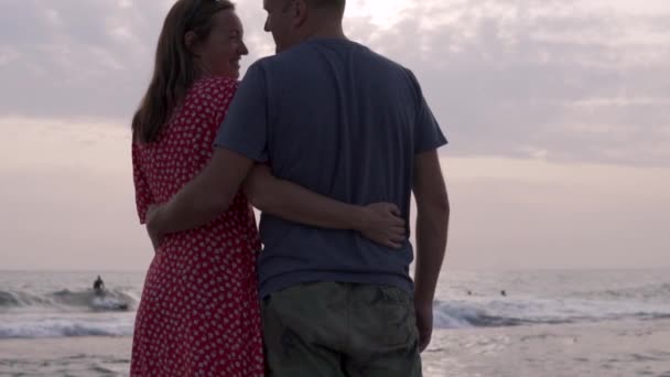 Arkadan bakınca, birbirine aşık bir çift gün batımında deniz kenarında birbirlerine sarılıyorlar. — Stok video