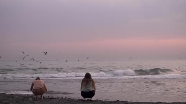 Egy nő fényképet készít egy nőről, aki a tenger felett repül naplementekor. — Stock videók