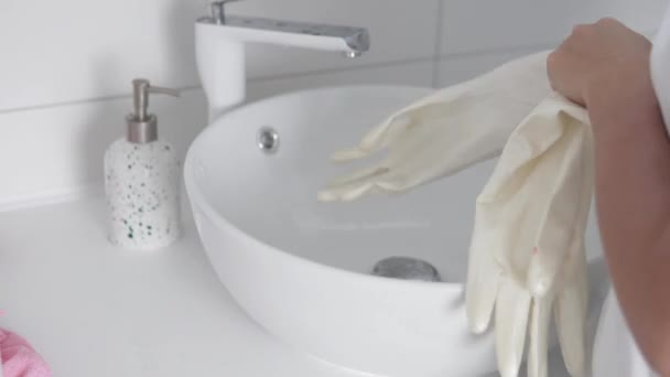 Домработница надевает перчатки и начинает мыть раковину в ванной с помощью чистящего средства — стоковое видео