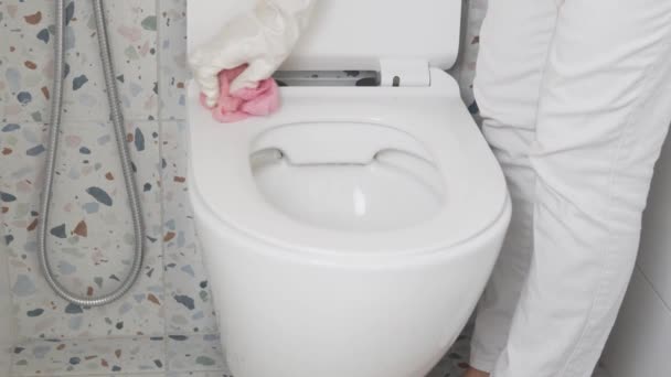 En hemmafru i handskar torkar toalettsitsen med en trasa — Stockvideo