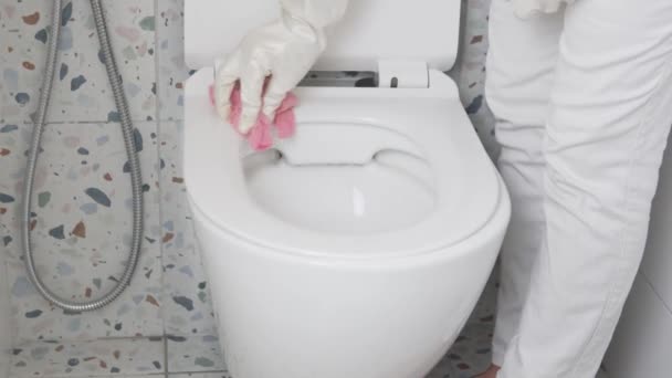 En kvinnlig hushållerska tvättar toalettsitsen med en trasa — Stockvideo