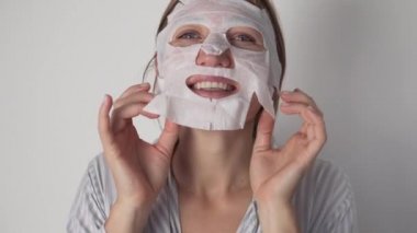 Neşeli bir kadın sabah yüzüne nemlendirici bir bez maske takar.