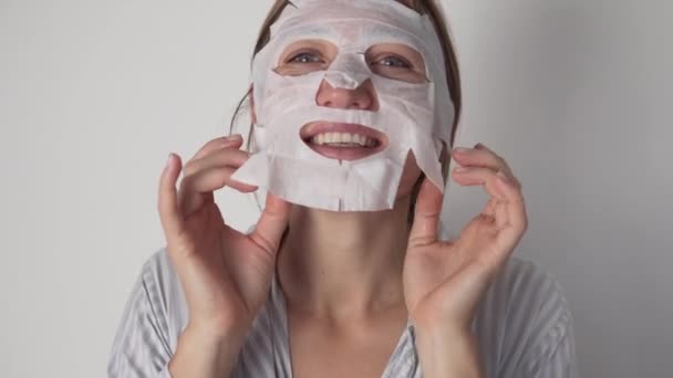 Веселая женщина надевает увлажняющую тканевую маску на лицо утром — стоковое видео
