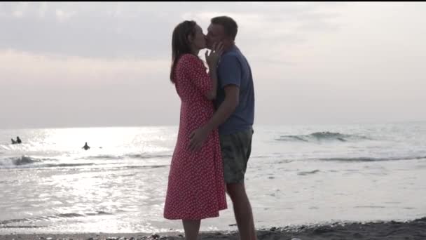 Влюбленные мужчина и женщина целуются у моря на закате — стоковое видео