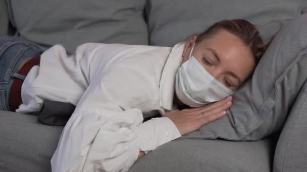 Een luie werknemer met een medisch masker op zijn gezicht valt op de bank en valt in slaap tijdens de lunch — Stockvideo