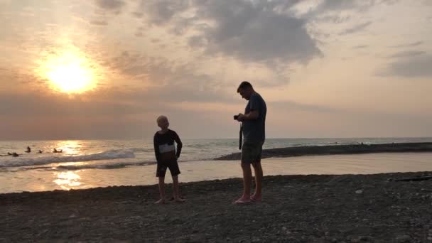 아버지는 해 가질 때 아들이 해변에서 찍은 사진을 찍는다. — 비디오