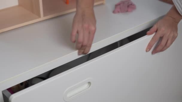 Een vrouw huisvrouw wast de stift uit een witte kast in de kinderkamer. — Stockvideo