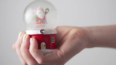 Bir kadın eli, yeni yıl ve Noel için cam bir kar küresi tutuyor.