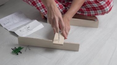 Talimatlara göre küçük bir ahşap rafı birleştiren kadın ellerinin yakın çekimi.