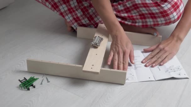 A mulher olha para as instruções e monta uma pequena prateleira de madeira para brinquedos no berçário — Vídeo de Stock