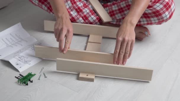 Una mujer conecta las partes de un estante de madera y lo monta utilizando pernos y un destornillador de acuerdo con las instrucciones — Vídeos de Stock