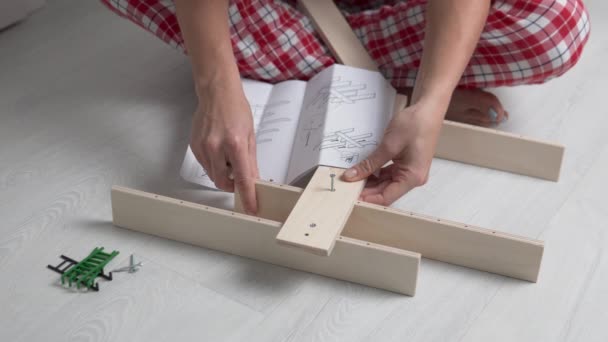 Жінка збирає за інструкцією дерев'яну полицю в дитячій — стокове відео