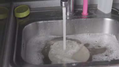 Koruyucu eldivenli eller mutfak lavabosunda kirli bir tava söyler.