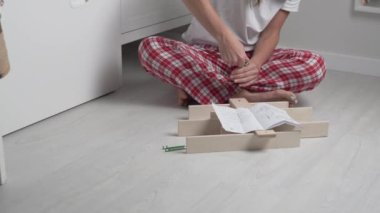 Noel pantalonlu bir kadın talimatlara göre çocuk odasında küçük bir ahşap raf topluyor.