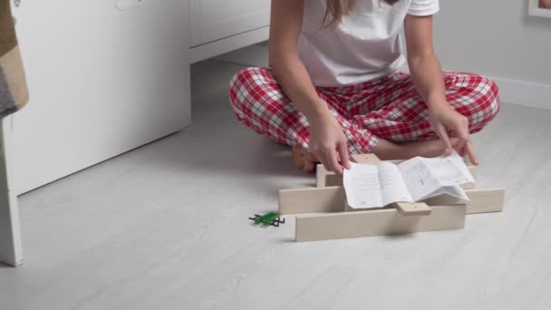 Женщина собирает деревянную полку для игрушек в детской комнате в соответствии с инструкциями — стоковое видео