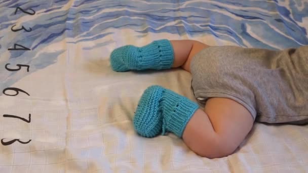 Close-up van de babybenen in gebreide slofjes op het bed — Stockvideo
