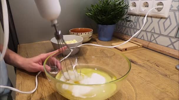 De mens slaat de eieren met suiker in een glazen bak met een blender — Stockvideo