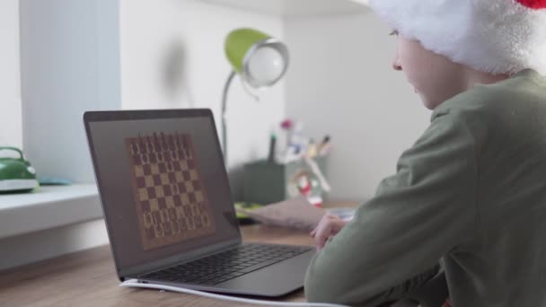 Um menino joga xadrez em casa com um computador durante as férias de Natal — Vídeo de Stock