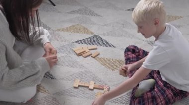 Bir kadın ve bir çocuk evde yerde domino oynuyorlar.