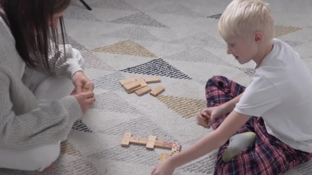 Egy nő és egy fiú dominózik otthon a földön. — Stock videók