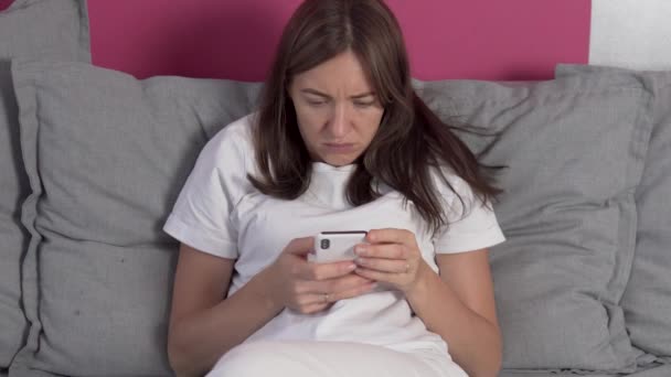 En kvinde bruger entusiastisk en mobiltelefon hjemme på sofaen – Stock-video