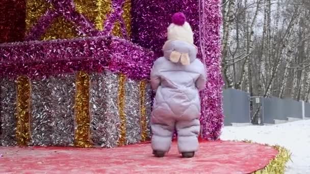 Een kind in een winterpak wandelt in de winter op een straatversierde scène in het park — Stockvideo