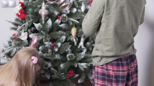 Starší bratr a jeho mladší sestra oblékají umělý vánoční stromek doma s hračkami — Stock video