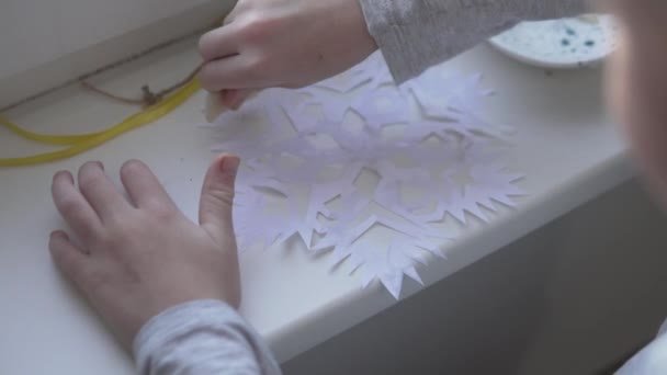 Ein Junge schmückt ein Fenster in einem Raum, der aus Papierschneeflocken geschnitzt ist — Stockvideo