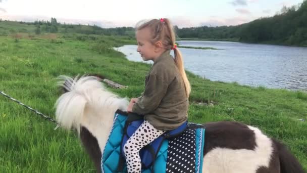 夏天，一个小女孩沿着河边骑着一匹小马 — 图库视频影像