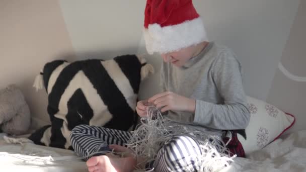 Ένα παιδί στο καπέλο του παππού του παγετού ξετυλίγει τη γιρλάντα της Πρωτοχρονιάς για το χριστουγεννιάτικο δέντρο — Αρχείο Βίντεο