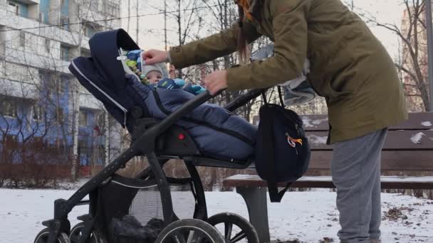 Egy anya egy babakocsiban sétál a babájával a ház közelében télen Oroszországban. — Stock videók