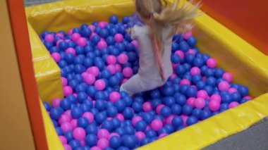 Güzel küçük kız havuza renkli toplarıyla atlıyor oyun merkezinde çocuklar için.