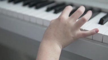 Elektronik beyaz piyano çalan çocuğun elinin yakın çekimi.