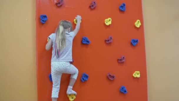 O fetiță se joacă pe un perete de cățărare într-o cameră de joacă pentru copii — Videoclip de stoc