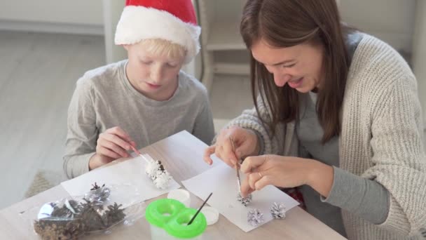 Nanny en jongen maken decoraties voor het huis van sparren kegels in de winter — Stockvideo