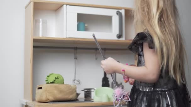 Vestida niña con una varita mágica cocina en la cocina de juguete de la casa — Vídeo de stock