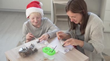 Anne ve oğlu Noel ağacını süslemek için beyaz ladin konileri boyuyorlar..