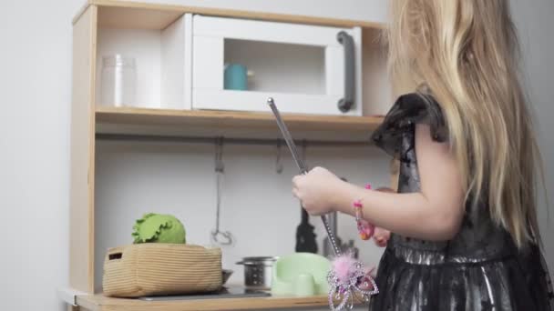 Öltözött kislány egy varázspálcával főz a játék konyha a ház — Stock videók