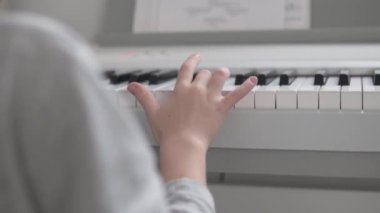 Yakın plan, notalarla hafif elektronik piyano çalan bir çocuğun elleri.